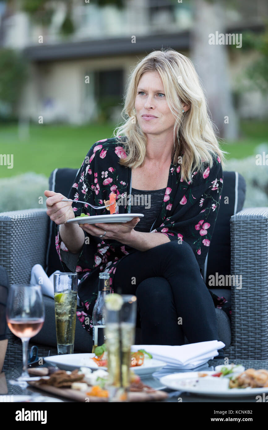 An attractive woman relaxes at an outdoor patio with food and drink while visiting the Kingfisher resort in Courtenay. Vancouver Island, British Columbia, Canada. Stock Photo