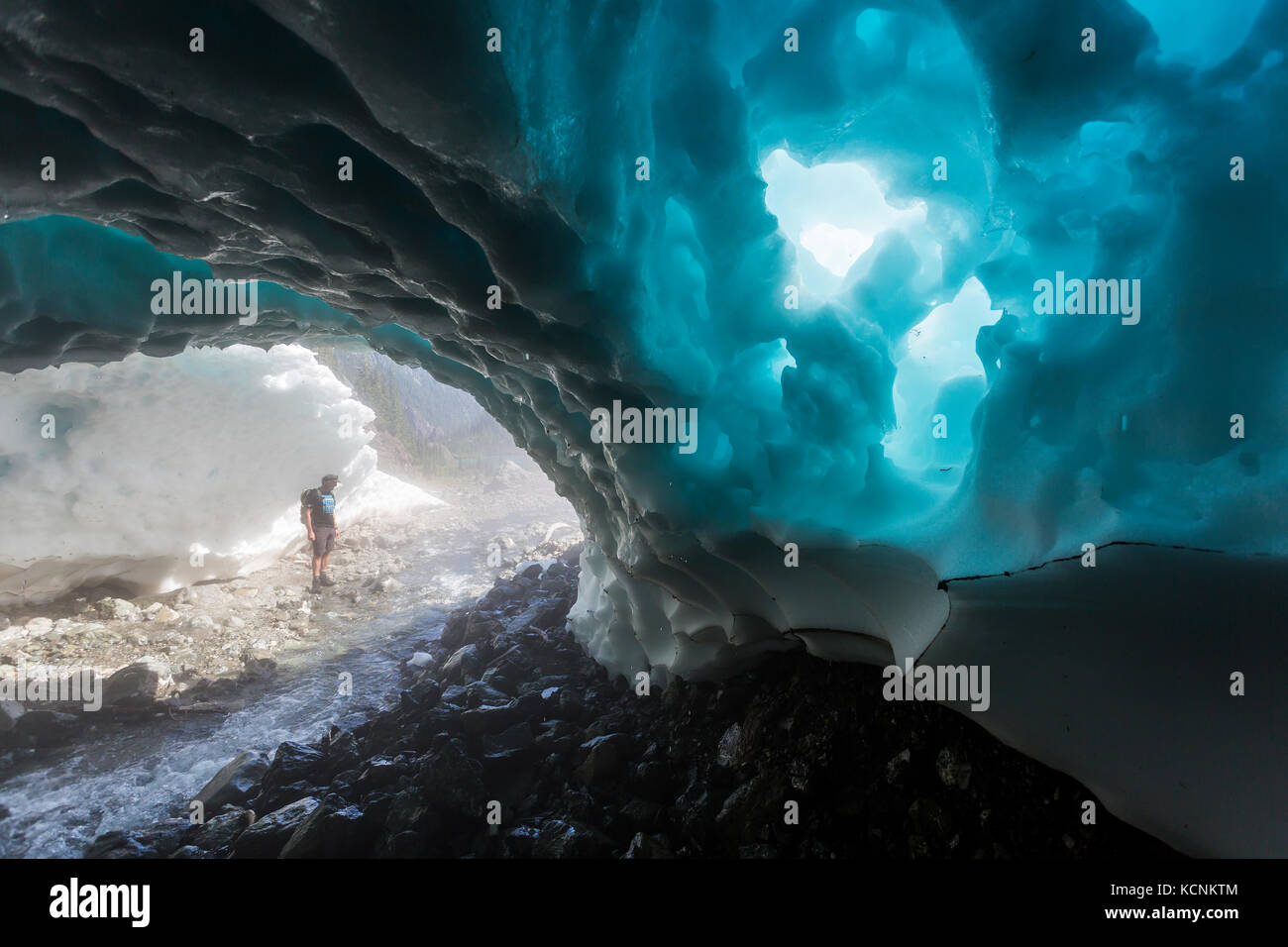 A hiker walks through a snow cave at the base of Century Sam lake, Strathcona Park, Vancouver Island, British Columbia, Canada. Stock Photo