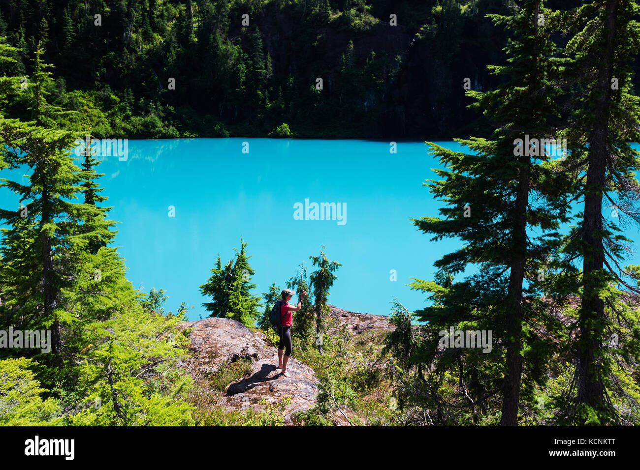 A female hiker stops to take in the view from a rock bluff overlooking Century Sam lake, Strathcona Park, Vancouver Island, British Columbia, Canada Stock Photo