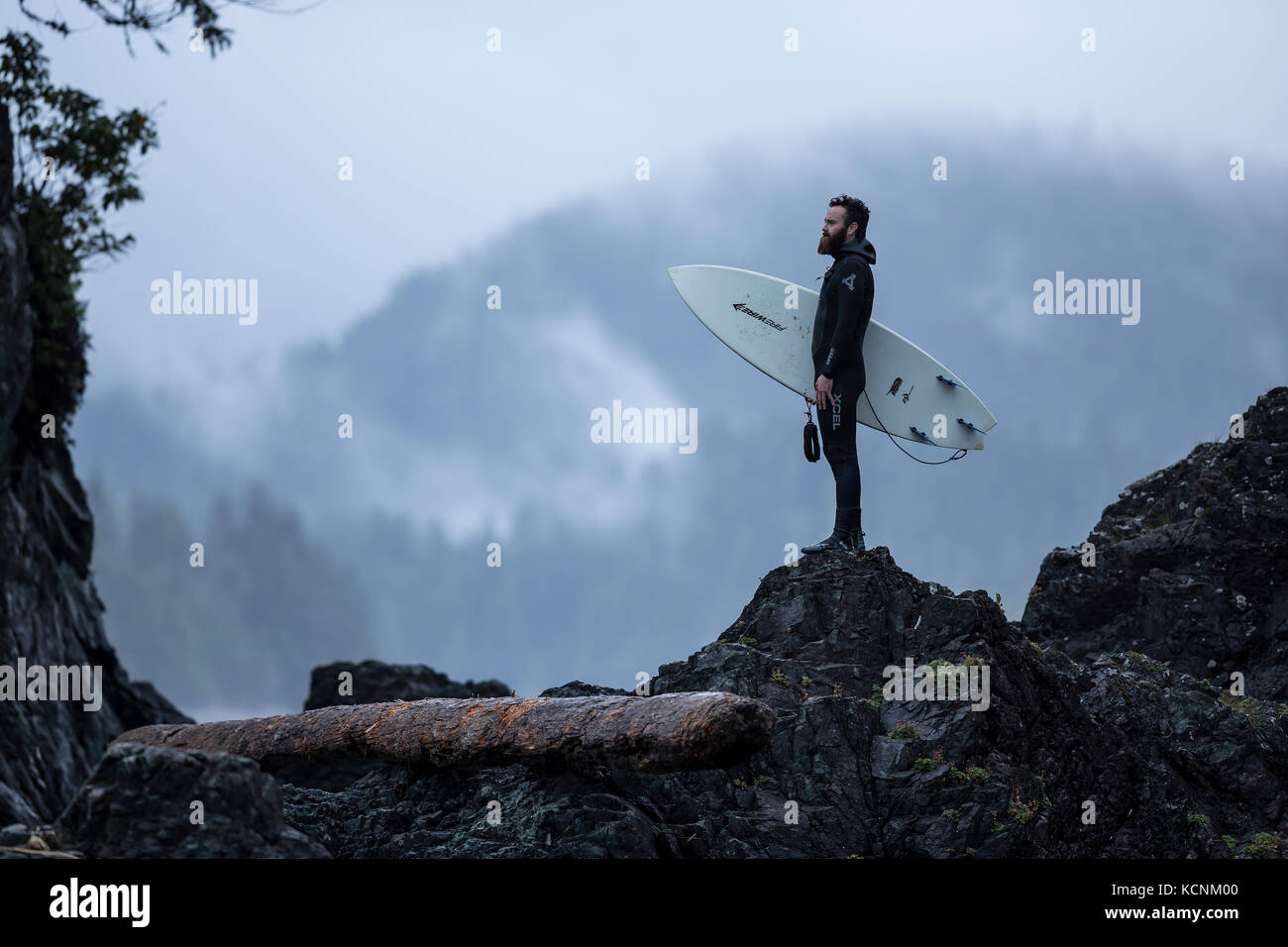 A surfer makes his way back to camp after a recon for waves on Spring Island's westernmost shoreline. Kyuquot, Vancouver Island, British Columbia, Canada Stock Photo