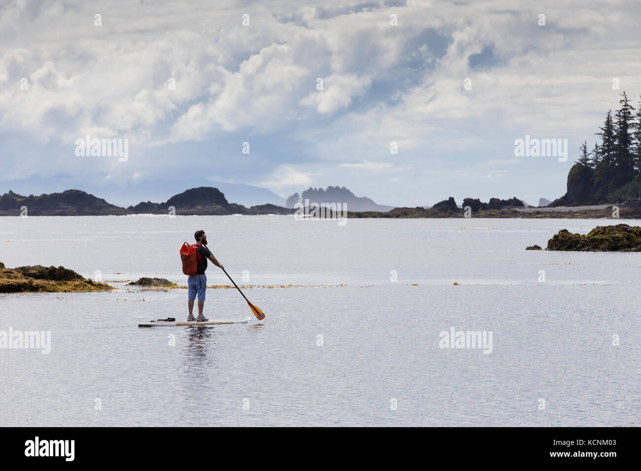 A stand up paddle boarder cruises the calm waters around Spring Island. Kyuquot, Vancouver