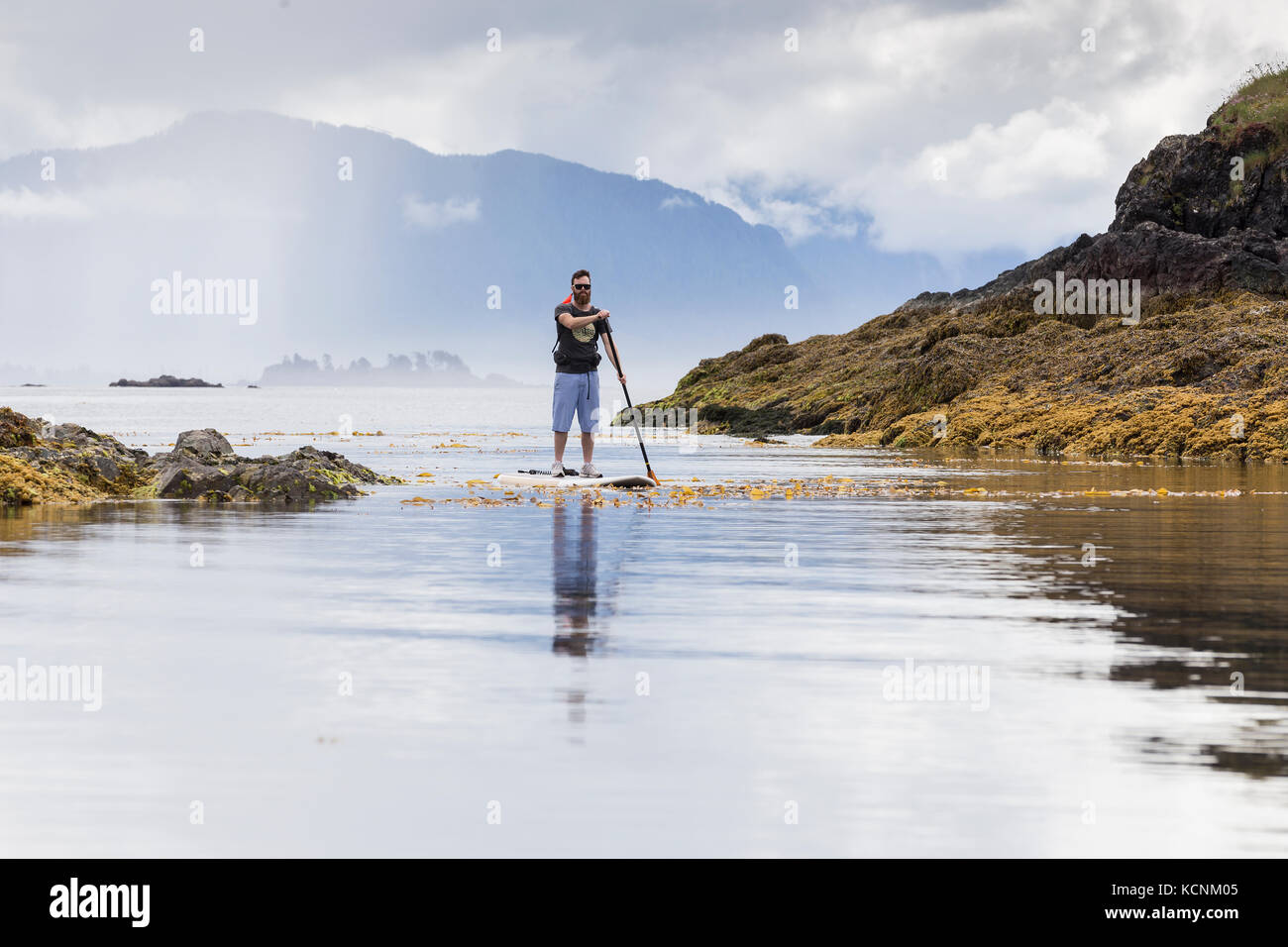 A stand up paddle boarder cruises the calm waters around Spring Island, Kyuquot, Vancouver