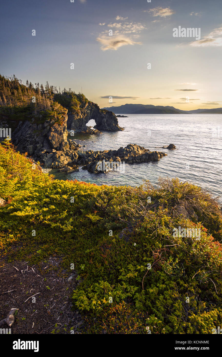 Sunset with a natural bridge in view along a coastal area of Green Bay near Langdon's Cove, Newfoundland & Labrador Stock Photo