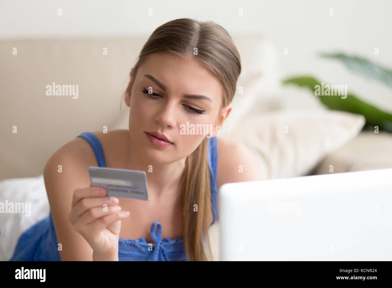 Young woman shopping online at home, holding credit card, paying on web