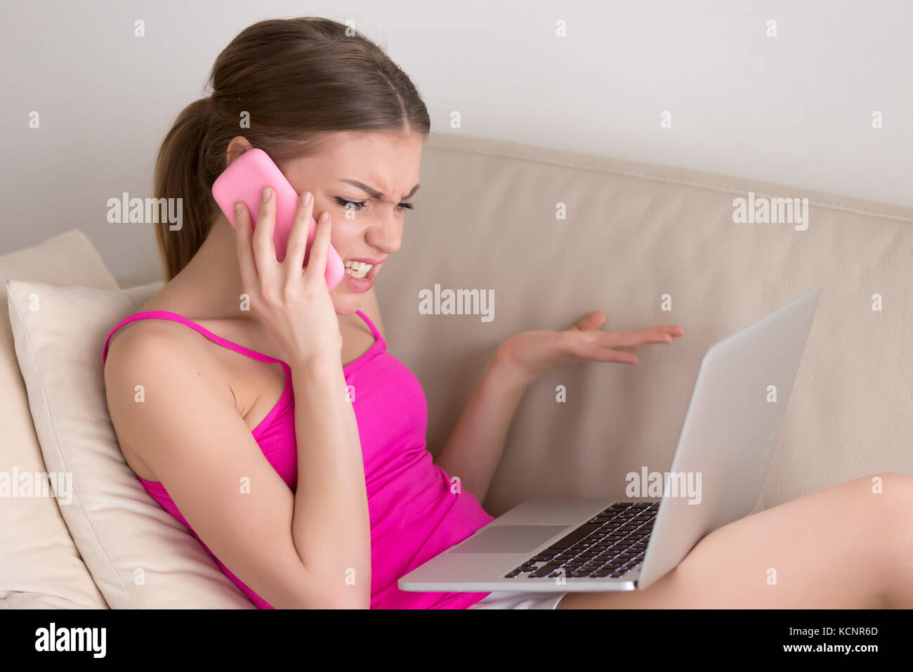 Angry mad young woman arguing on cellphone about broken laptop problem sitting on sofa at home, furious disgruntled customer calling service support c Stock Photo