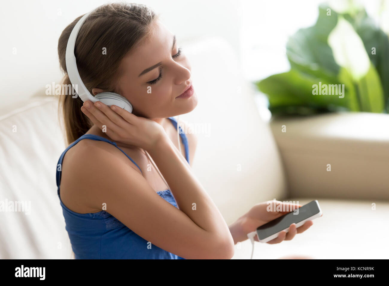 Relaxed calm young woman enjoys music, teenager wearing headphones listens to high quality sound using player application on smartphone, teen girl med Stock Photo