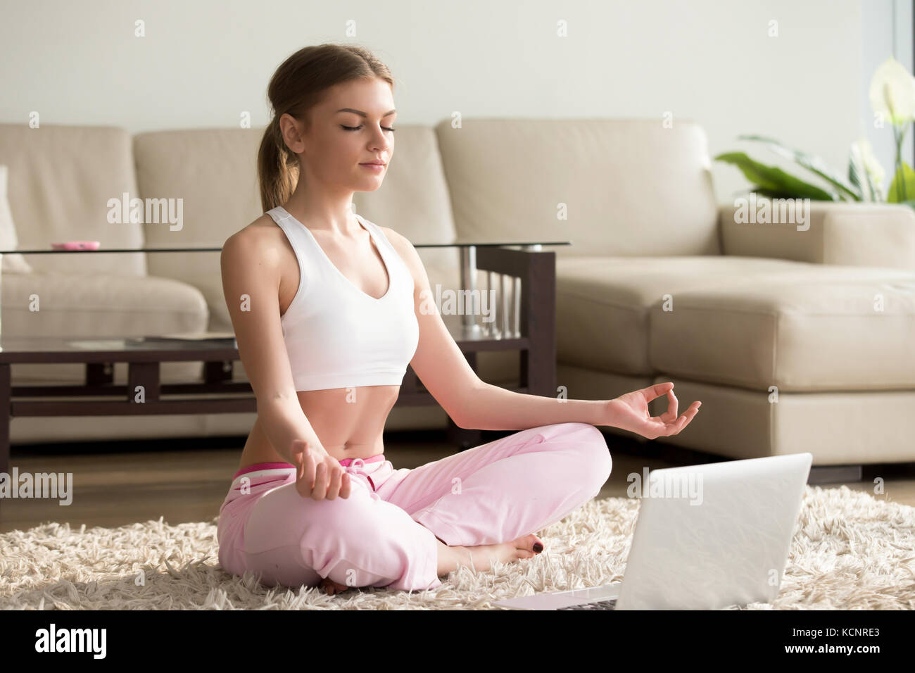 Young calm woman sits in staff easy lotus pose near laptop at home ...