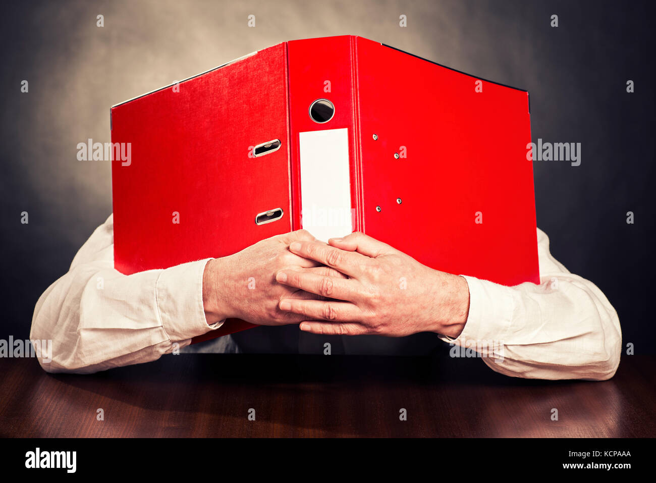 An employee hides his face behind a red file folder. Stock Photo