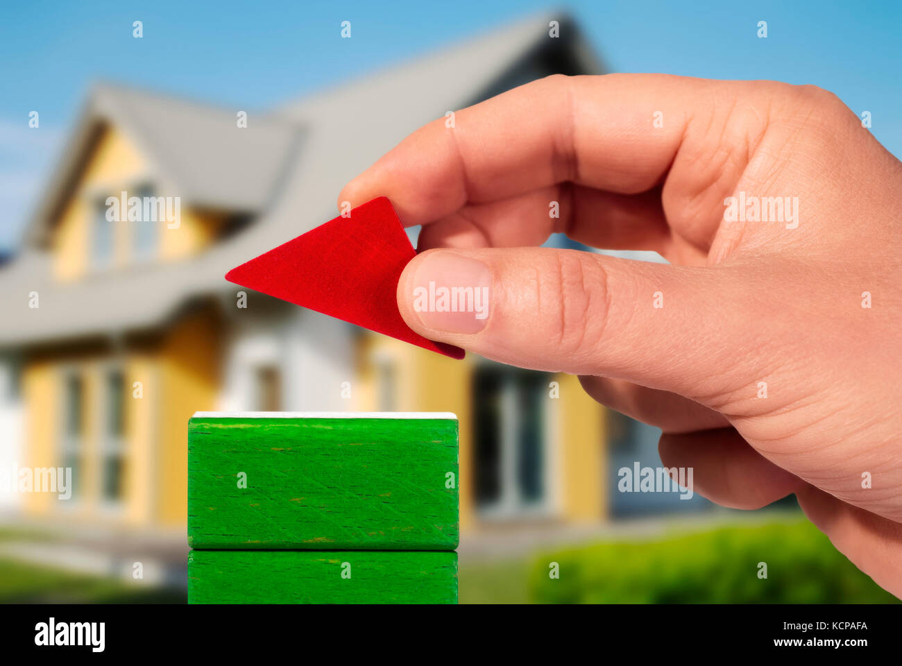 Hand with building bricks and house in the background Stock Photo