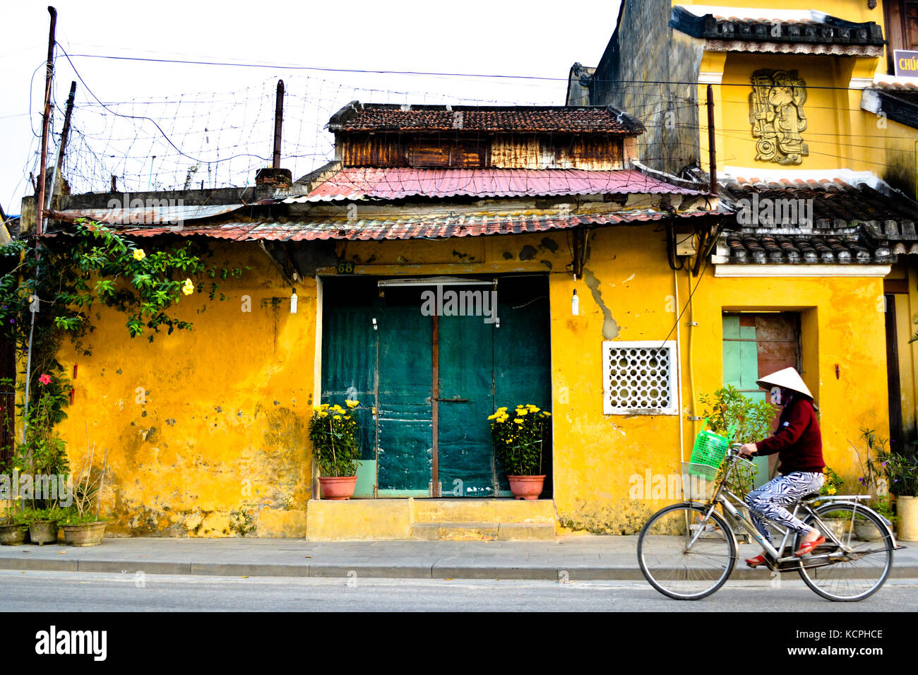 Vietnamese Women on Bike in Front of Yellow Building Stock Photo