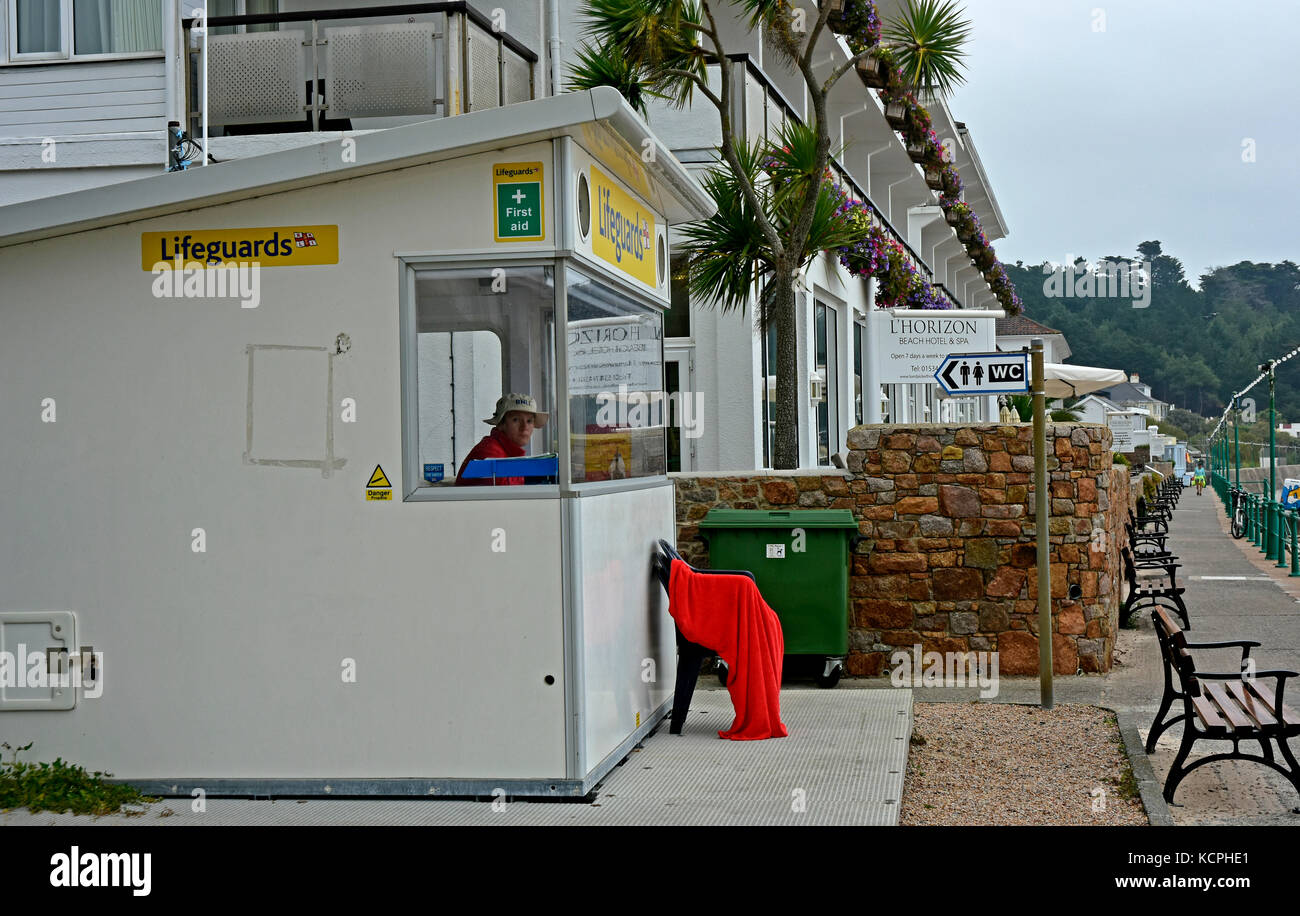 St Brelade's Bay - Jersey - Channel Isles - Lifeguards on shore station - guard on duty - bored - no action -deserted promenade - red towel on a chair Stock Photo