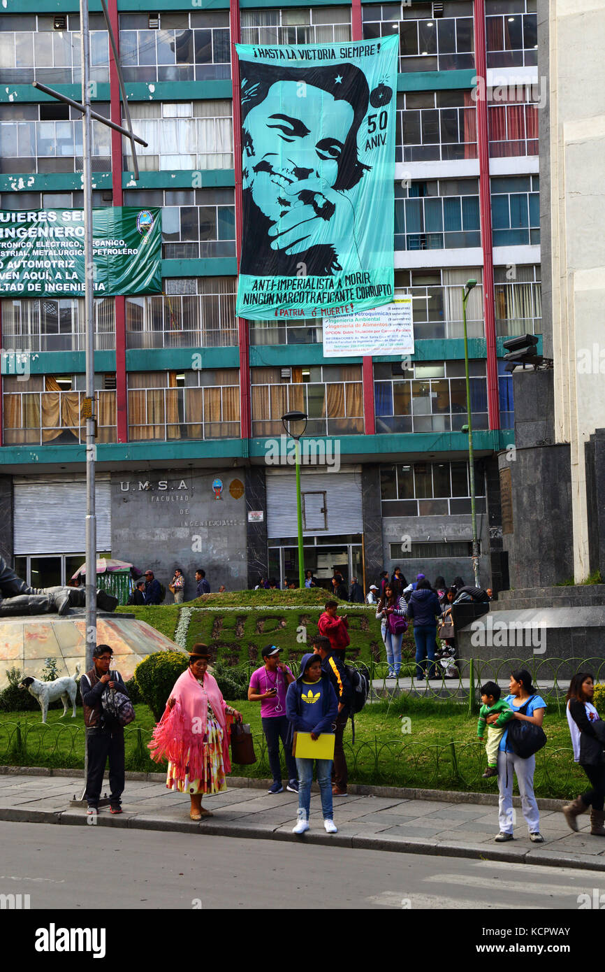 La Paz, Bolivia. 6th Oct, 2017. A banner to commemorate the 50th anniversary of Che Guevara's death hangs on the UMSA University Engineering Faculty building in La Paz city centre. Che was killed by Bolivian troops in La Higuera on 9th OCtober 1967; the government and social movements will be holding various events on that date at the location. In the foreground an Aymara woman wearing traditional dress is standing on the pavement Credit: James Brunker / Alamy Live News Stock Photo