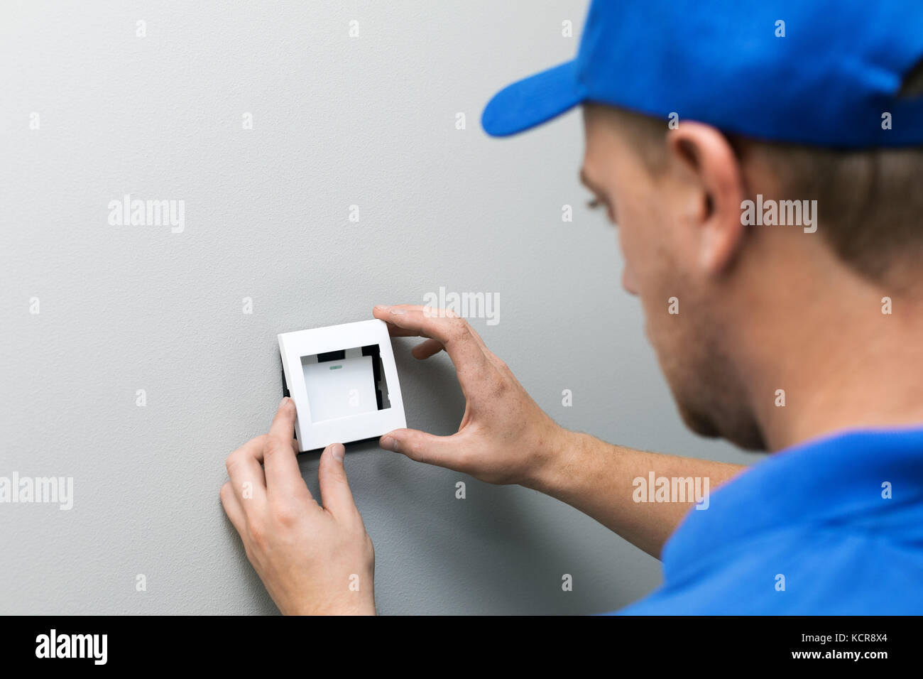 electrician in blue uniform installing light switch on the wall Stock Photo