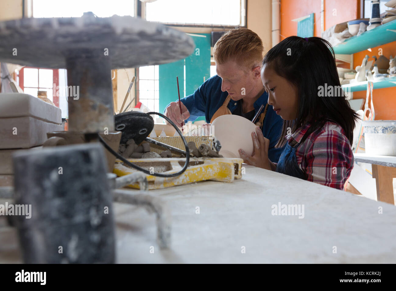 Male potter and girl painting bowl in pottery workshop Stock Photo - Alamy