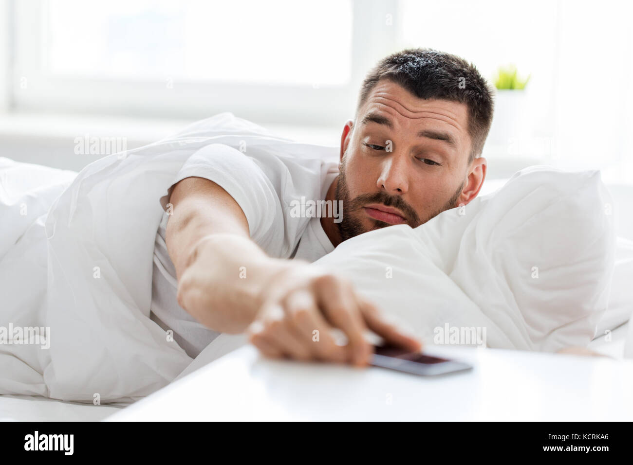 young man reaching for smartphone in bed Stock Photo - Alamy