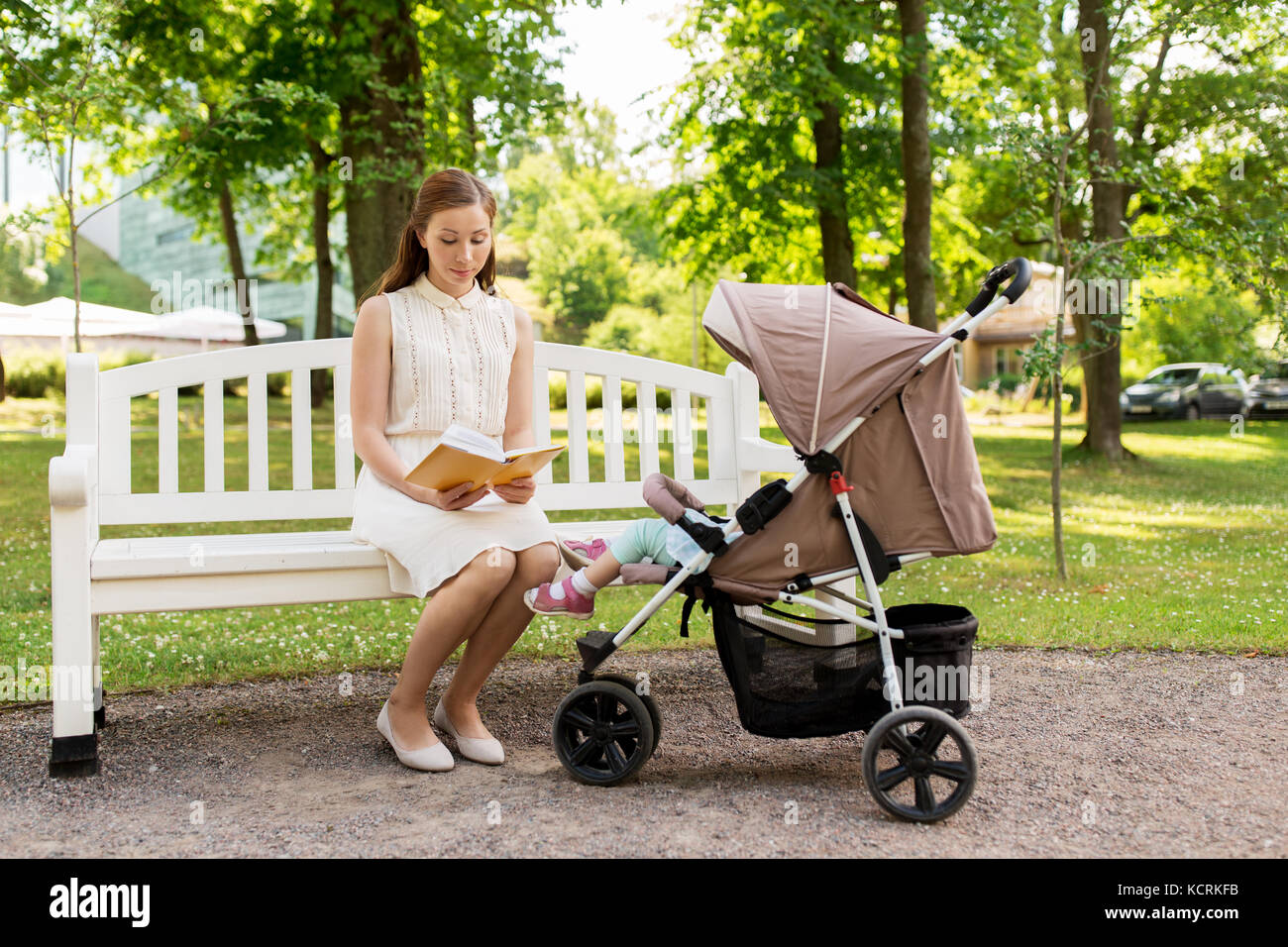 mother with child in stroller reading book at park Stock Photo