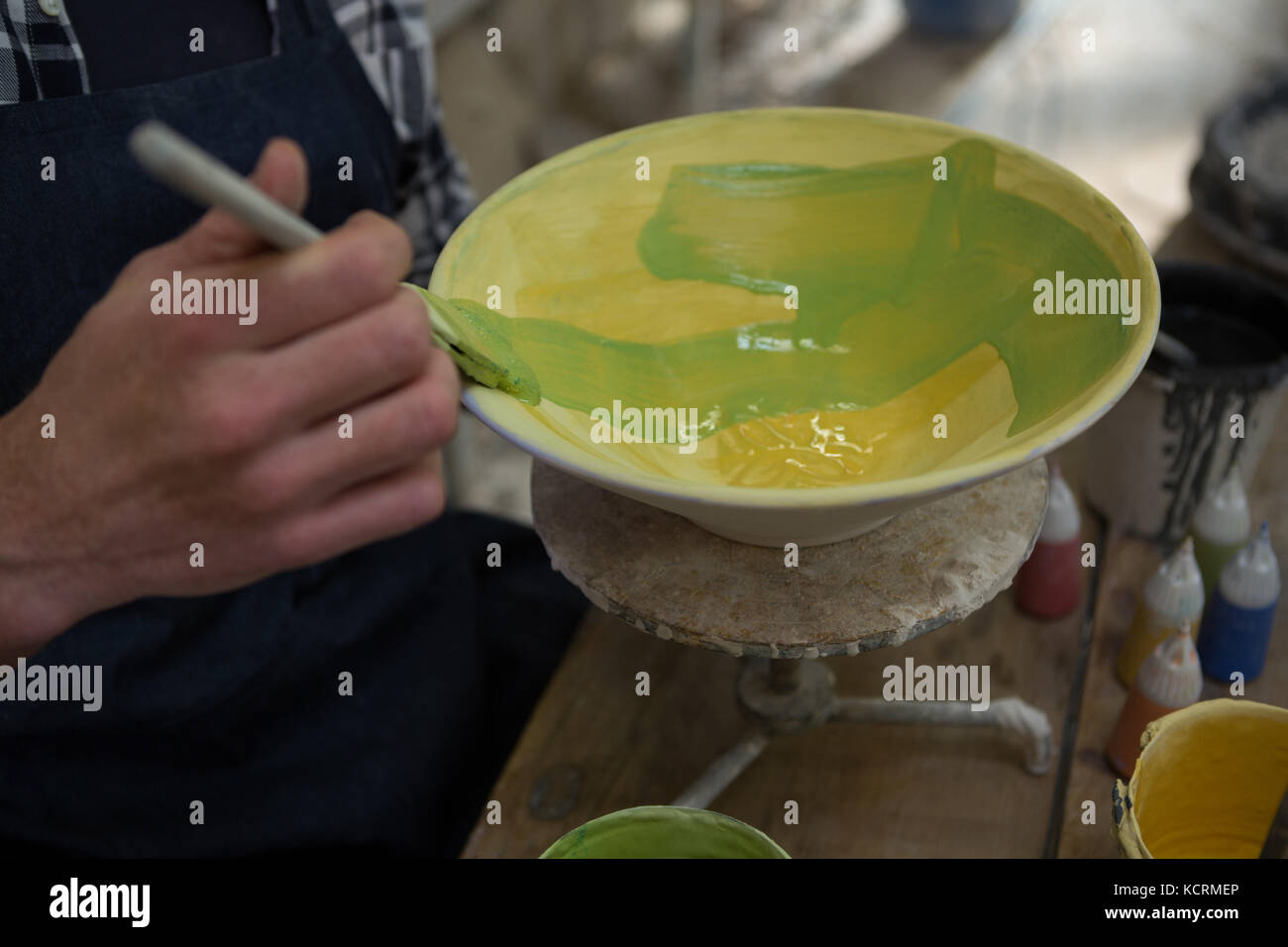 Mid-section of male potters hand painting a bowl in pottery workshop ...
