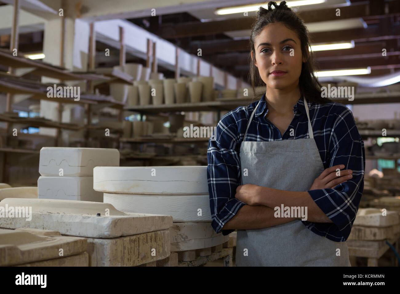 Portrait of female potter standing with arms crossed in pottery ...