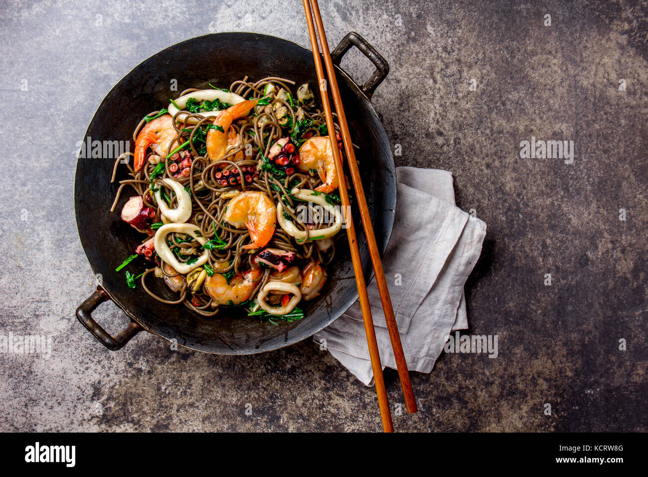 Buckwheat stir-fry noodles with seafood - shrimps, octopus, squid in cast  iron asian wok with cooking chopstick. Top view, stone background Stock  Photo - Alamy
