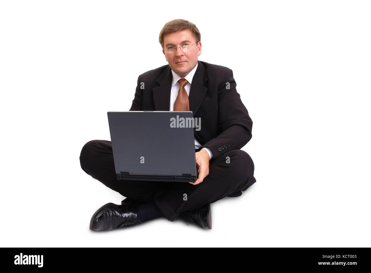 Young businessman in black suit sitting cross-legged with laptop over ...