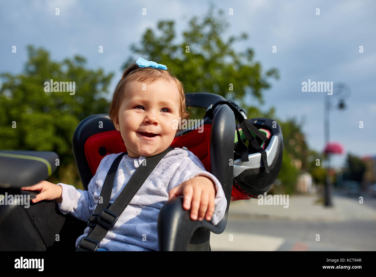 Closeup cute happy little baby on bike seat cycling in city park Stock