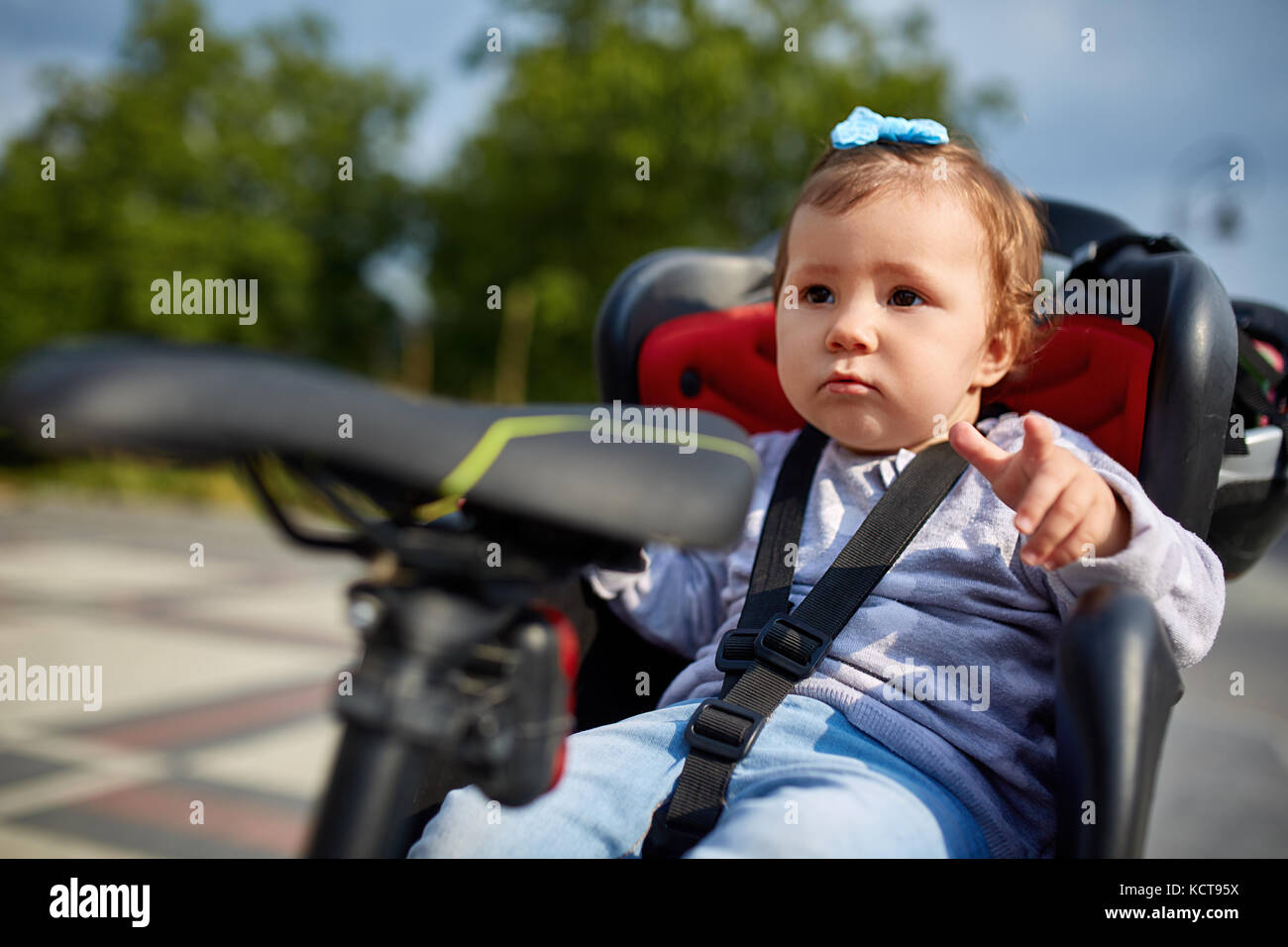 Closeup cute happy little baby on bike seat cycling in city park Stock