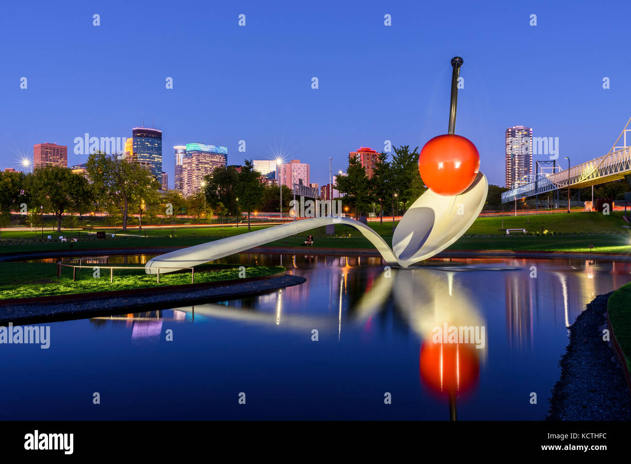 Spoonbridge and Cherry sculpture in front of Minneapolis skyline at nightt. Designed by Claes Oldenburg and his wife, Coosje van Bruggen. The complex  Stock Photo