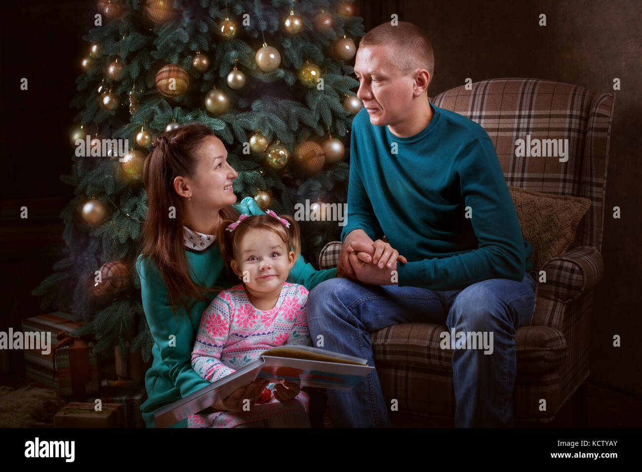 Young family near the Christmas tree. Mother and daughter look the book Stock Photo