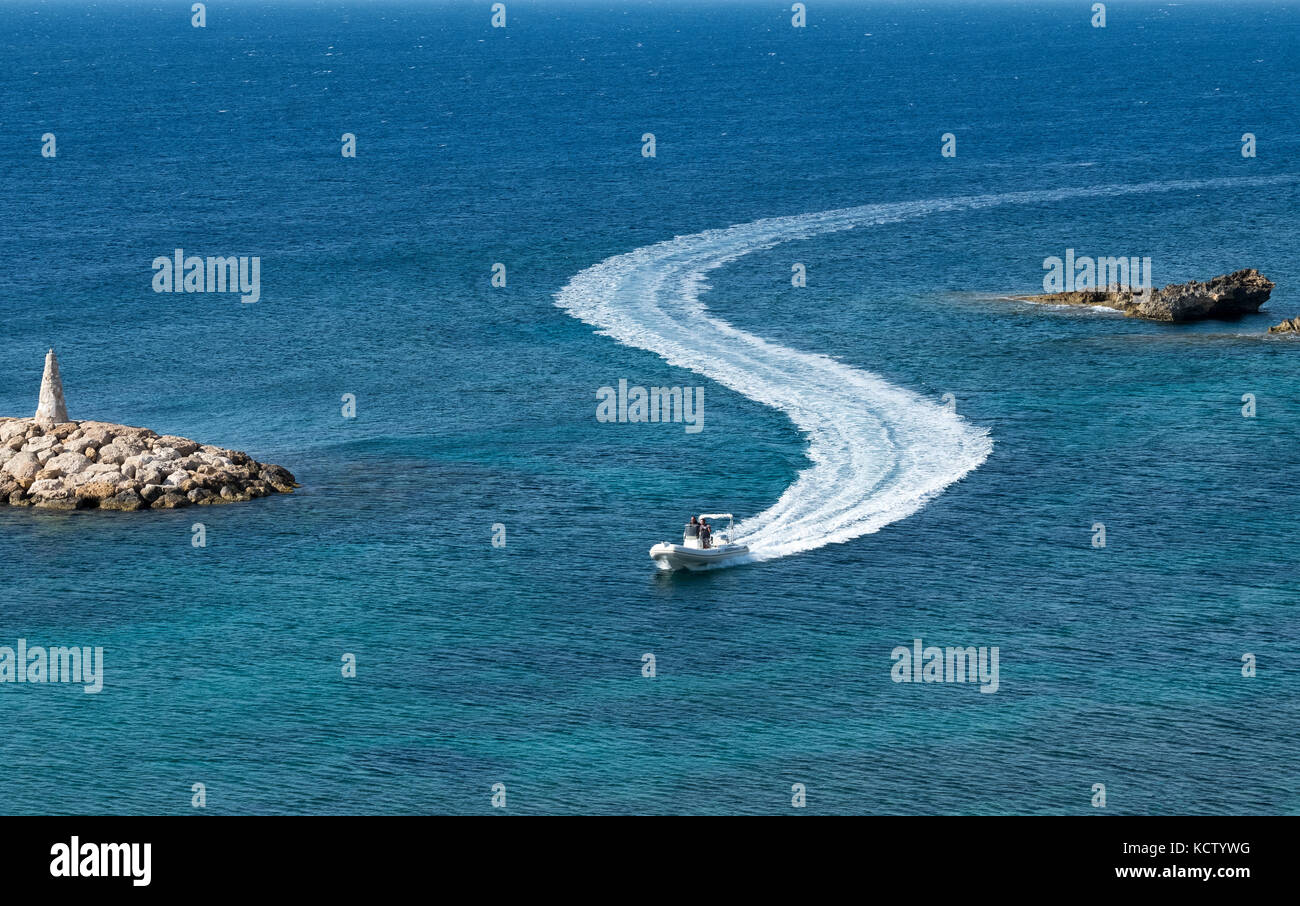 A  small vessel leaves an S shaped wake as it enters St Georges harbour near Paphos in Cyprus. Stock Photo