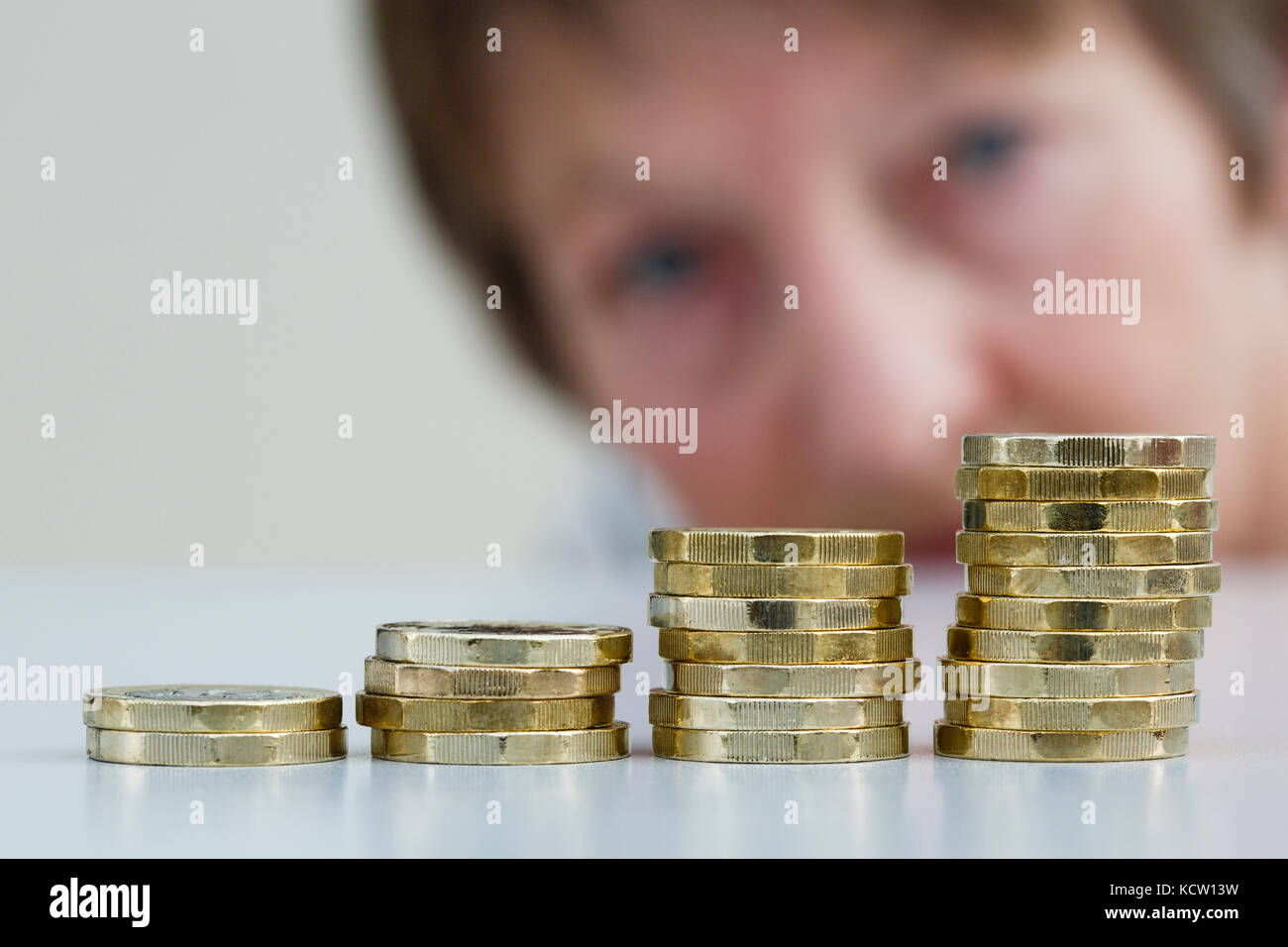 A pensioner looking concerned at a pile of British money pounds sterling new pound coins GBP in four piles. Watch savings grow investments concept UK Stock Photo