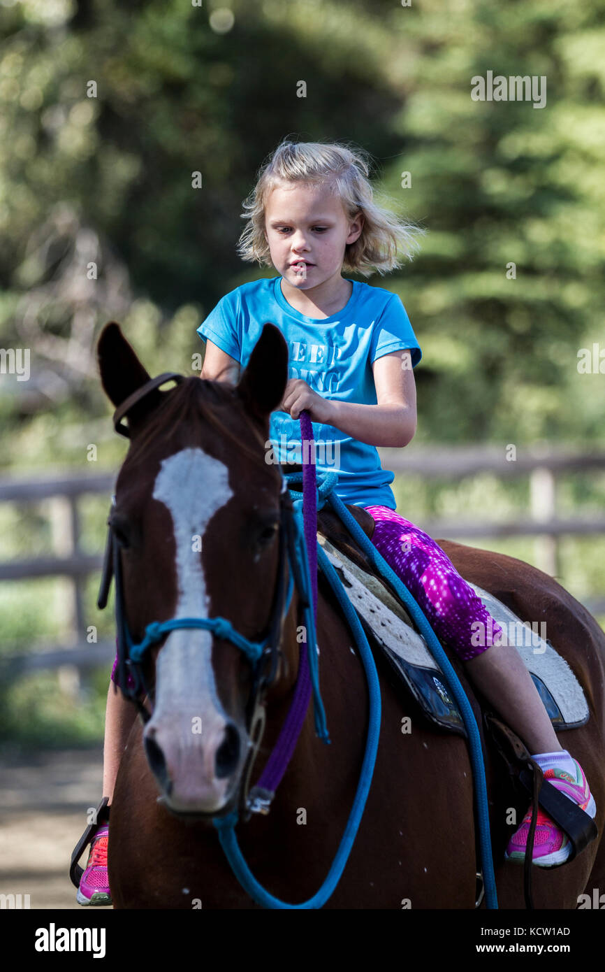 Young blonde girl, concentrating on ridng horse, coming at camera
