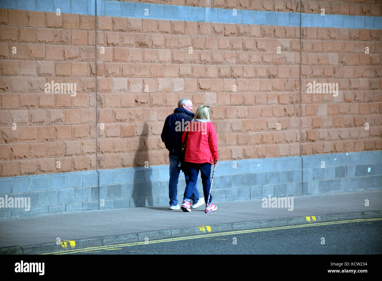 older couple with wall background walking on street  pavement viewed from behind Stock Photo