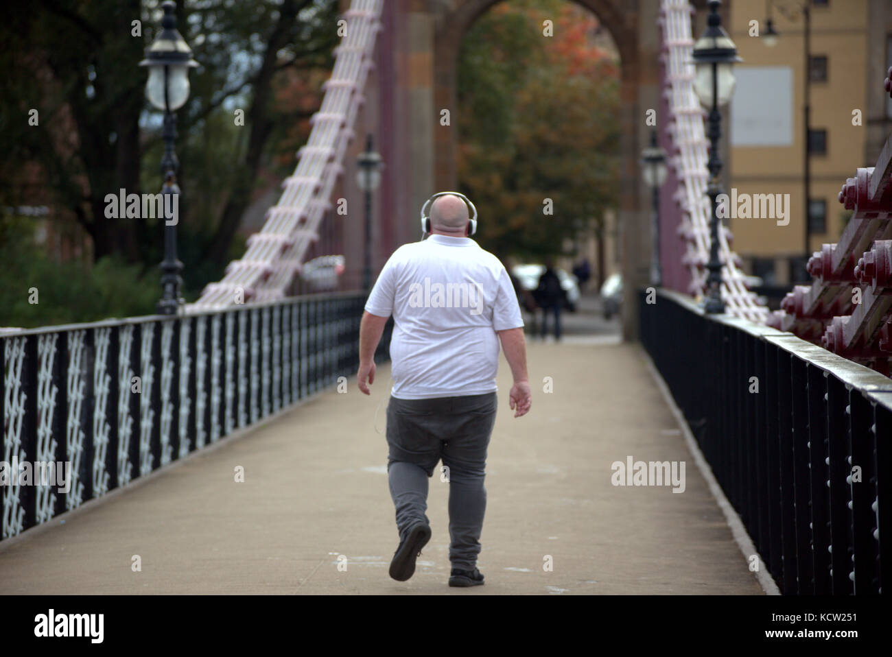 man male listening to music overweight fat unhealthy walking crossing bridge Stock Photo