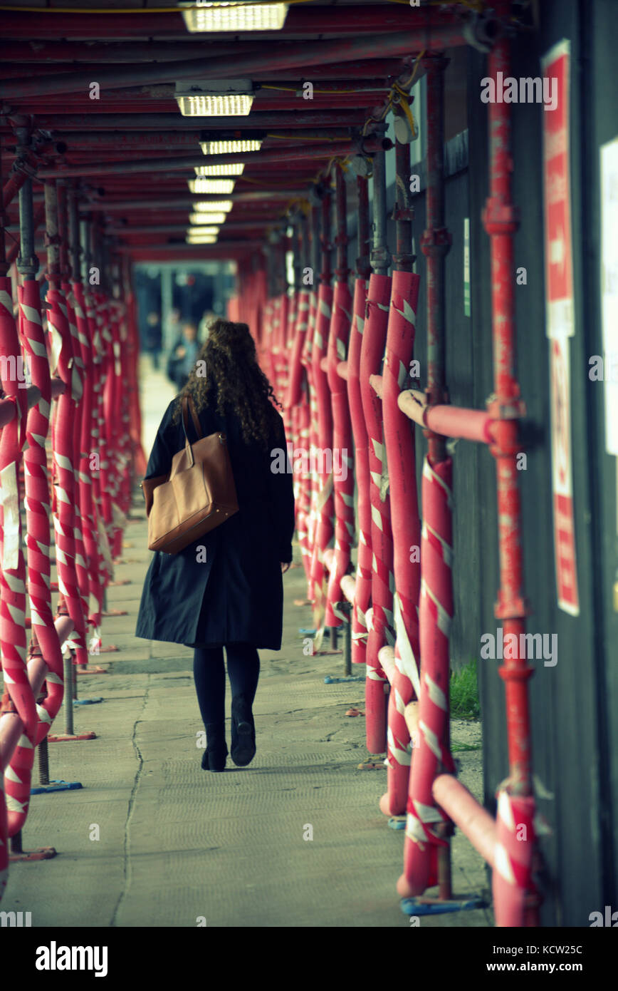 scaffolding red tunnel girl  distant male figure walking through viewed from behind city scene street Stock Photo