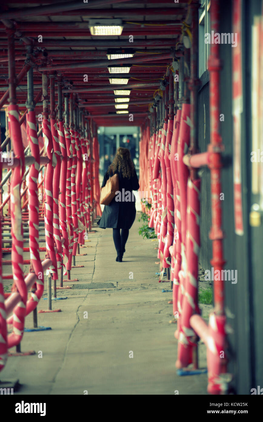 scaffolding red tunnel girl young woman  walking through viewed from behind city scene street Stock Photo