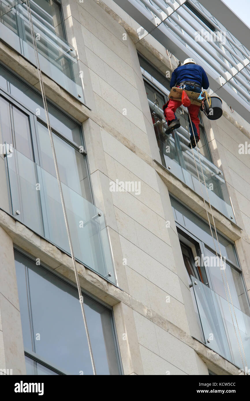 Window washer washing office building windows hanging outside the building on ropes Stock Photo