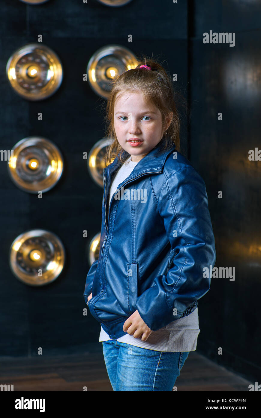 Modern little girl in a leather jacket posing on a glowing background ...