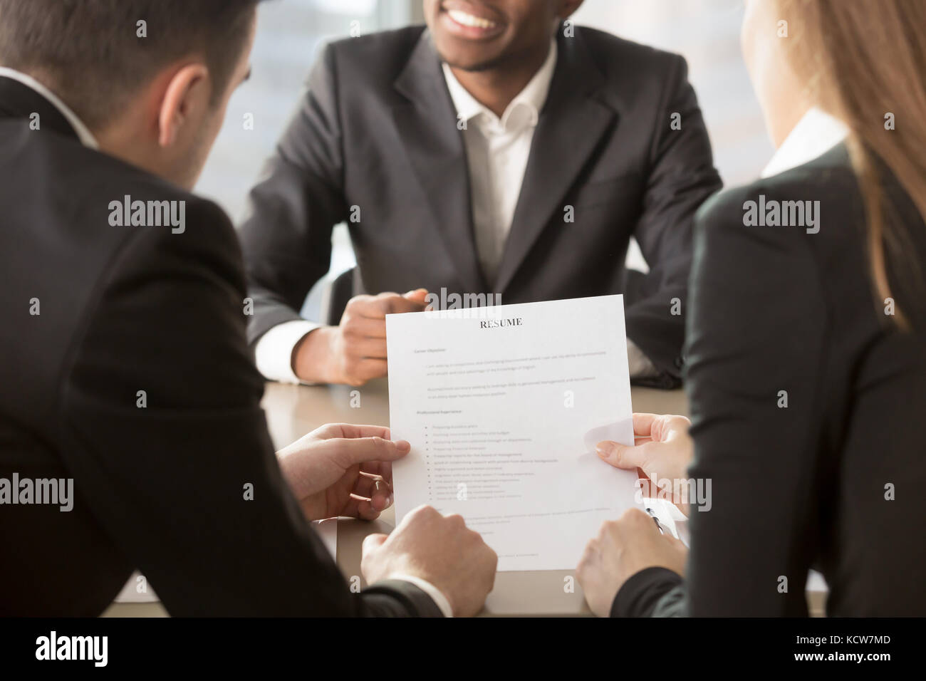 HR managers analyzing resume, asking afro american applicant about skills, actual work experience. Recruitment agency hiring specialist, conducting in Stock Photo