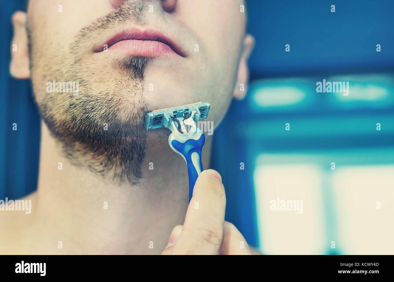 Young man shaves his short beard shaving machine tool. Half face with a