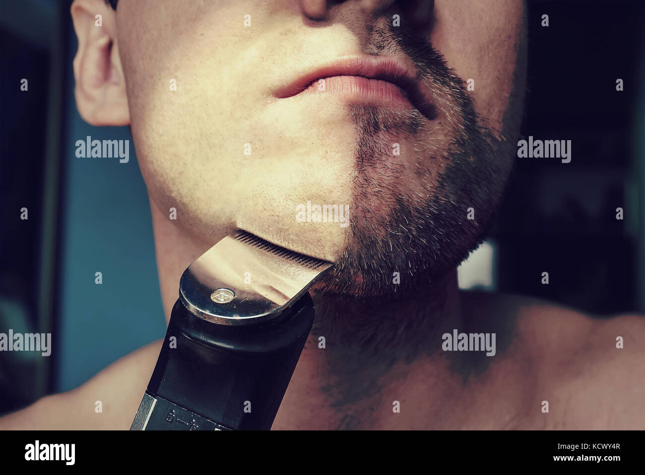 a man mowing a beard with hair clippers hair. Half face with a beard half shaved. Stock Photo