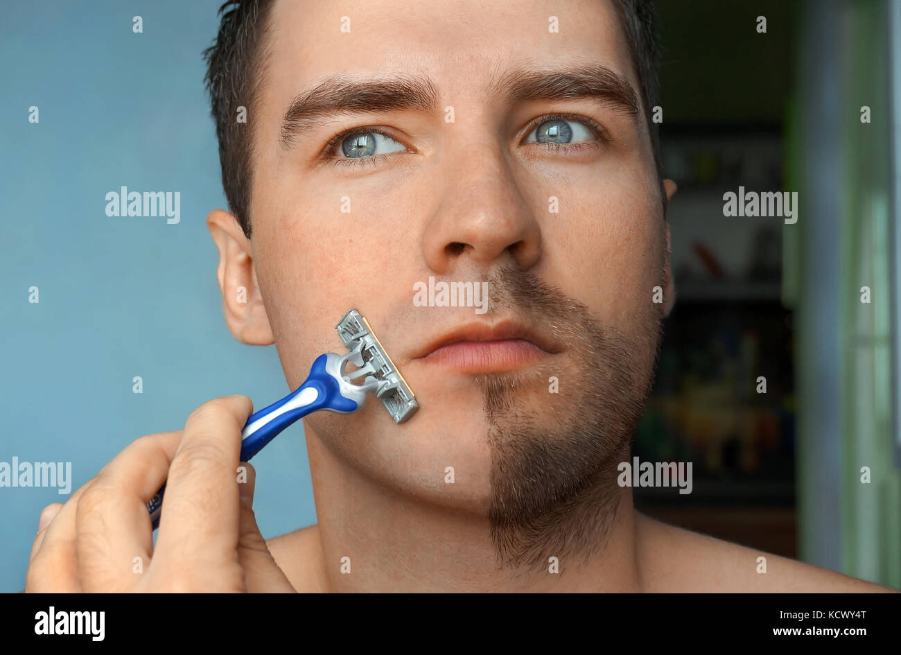 a nice young man shaves his beard. Half face with a beard half shaved. Stock Photo