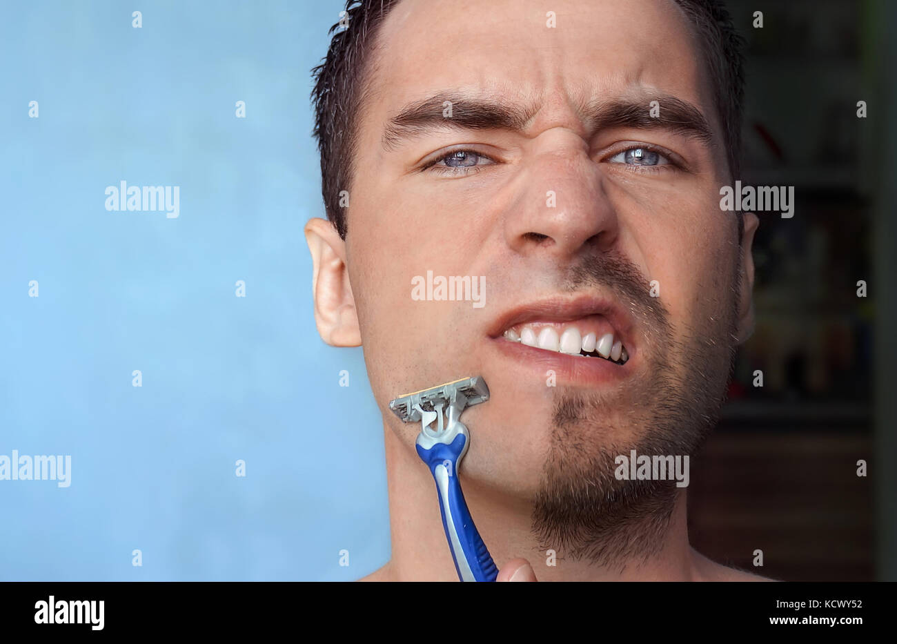 A man shaves his face without cream or foam, experiencing pain and