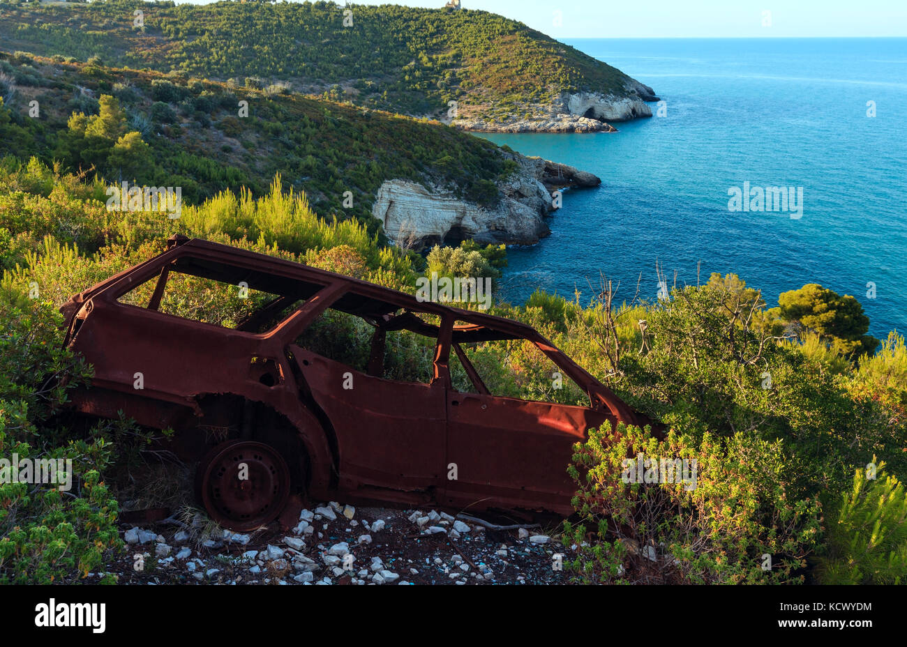 Broken demage rusty car on summer sea coast hill near Arch of San Felice on the Gargano peninsula in Puglia, Italy Stock Photo