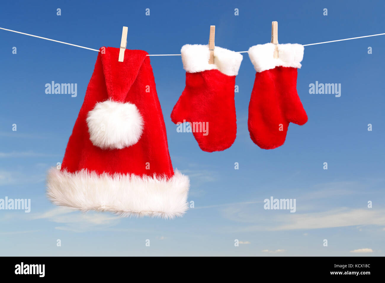 Red santa claus hat and pair of gloves drying in the open air hanging on clothes line affixed with wooden pegs Stock Photo