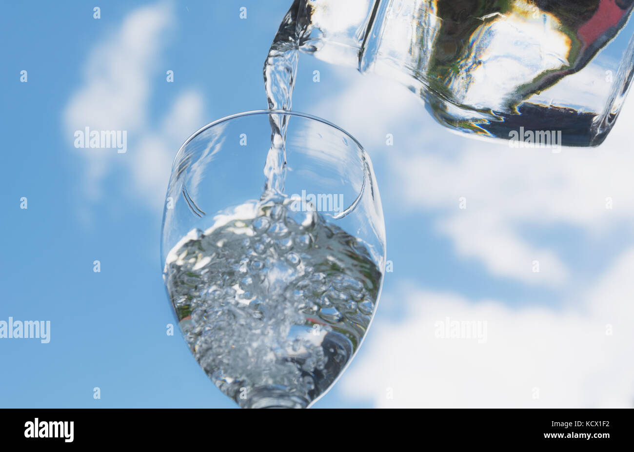 Female hand pouring water from bottle to glass with blue sky background. Stock Photo