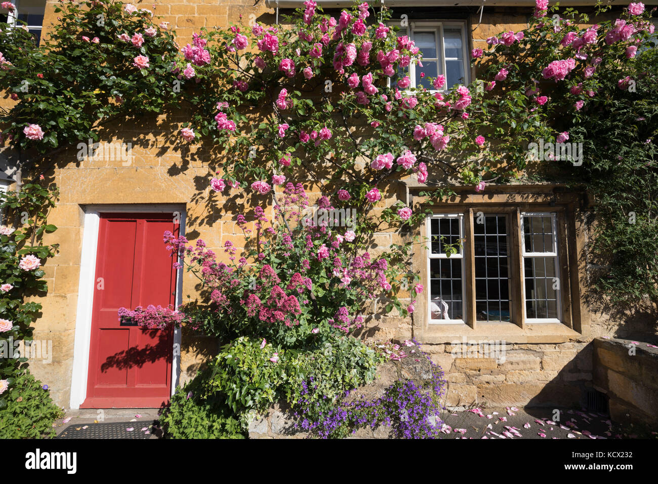 Rose Covered Frontage Of Cotswold Stone Cottage Along High Street