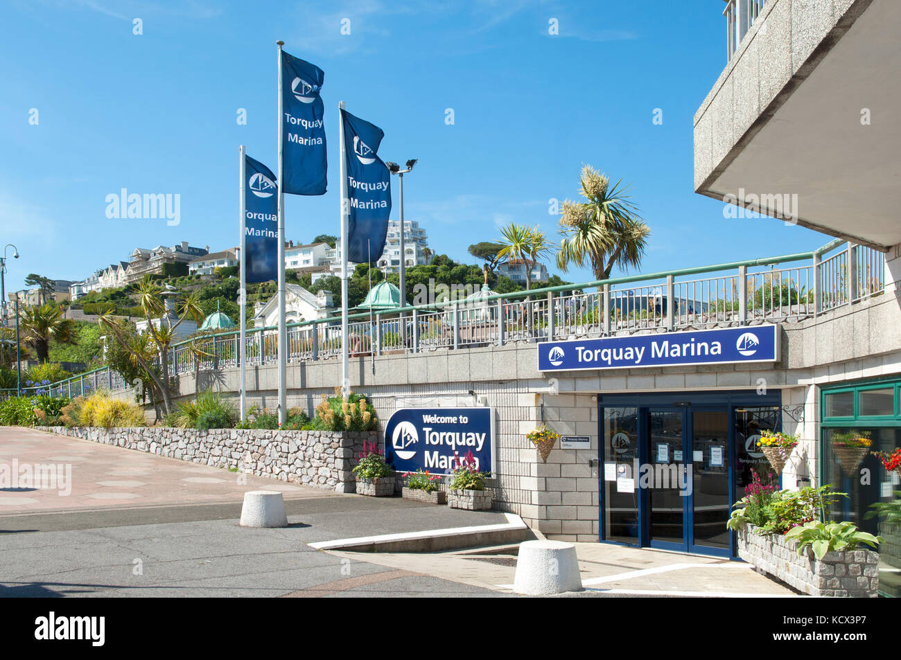 Entrance to MDL Marina on Torquay Harbourside, summer day, flags flying, promenade and railings. Seafood Coast Stock Photo