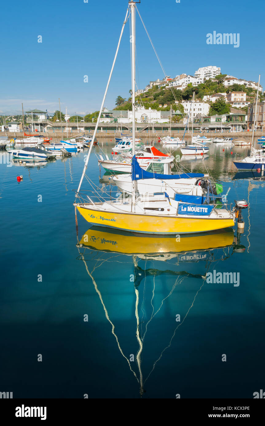 Small yellow sailing boat moored in Torquay marina. Summer day, reflection of boat in calm water, blue sky and sunshine. Portrait Copy space Stock Photo