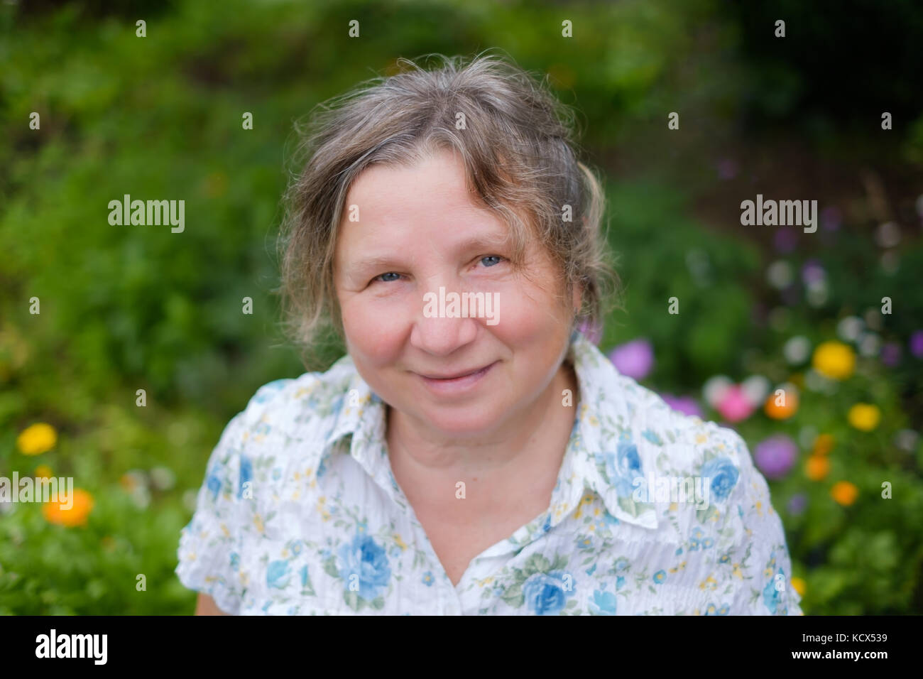 Portrait of caucasian mature cheerful mature woman standing outdoors in garden. She is smiling. Stock Photo