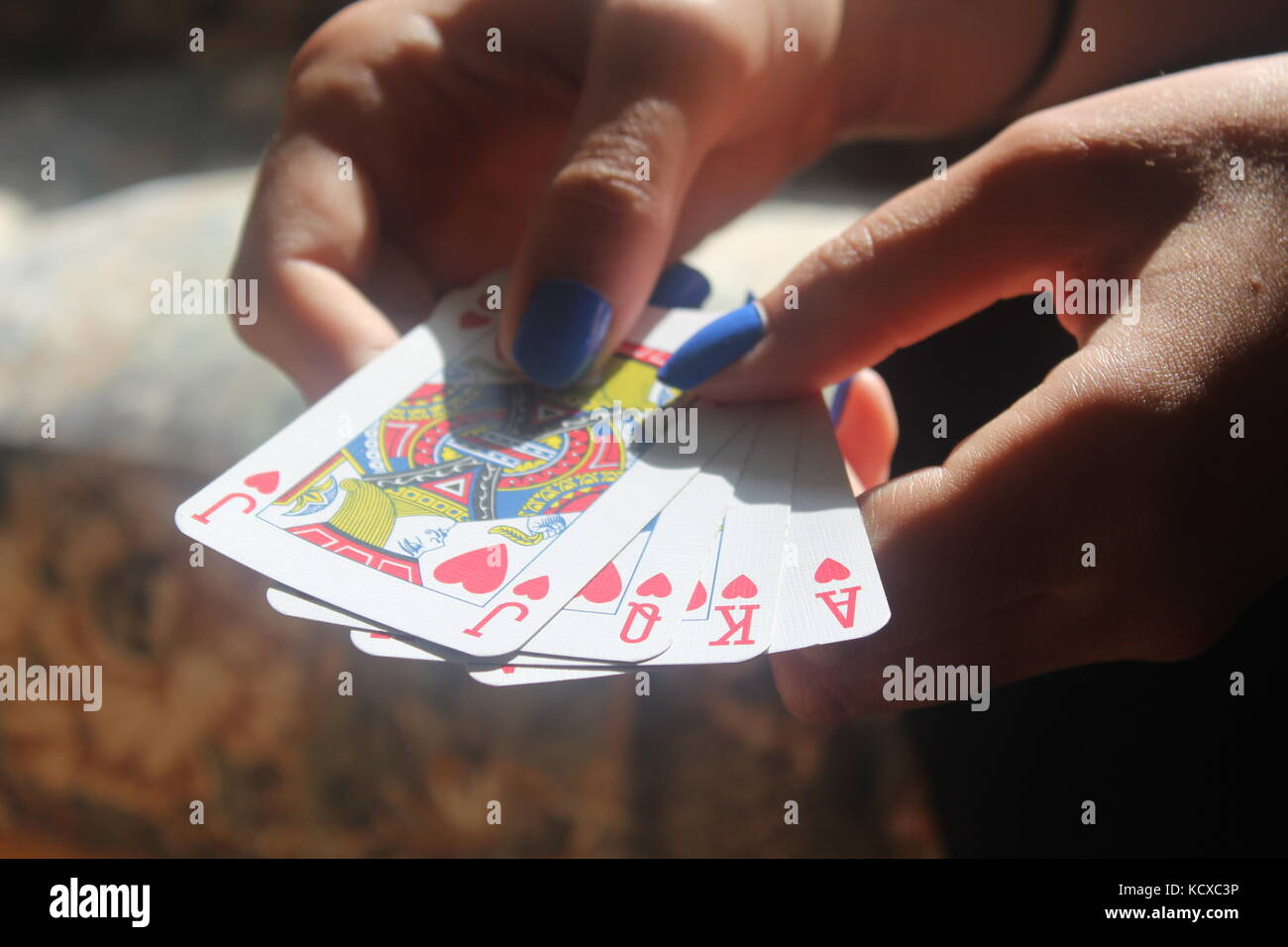 Female hands with blue fingernails spread pack of blue playing cards on wooden table. Stock Photo